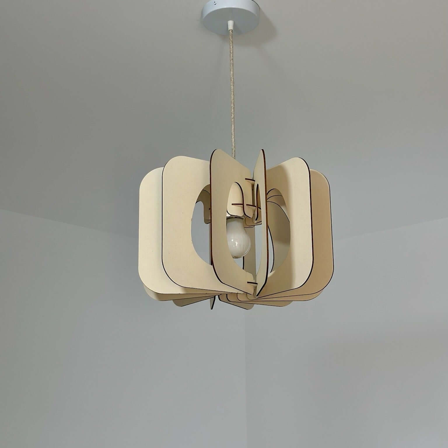 Suspension lumineuse en bois clair, au design moderne et épuré, illuminant une pièce avec un jeu subtil d'ombres projetées au plafond. Ses formes organiques et arrondies apportent une touche d'élégance naturelle.