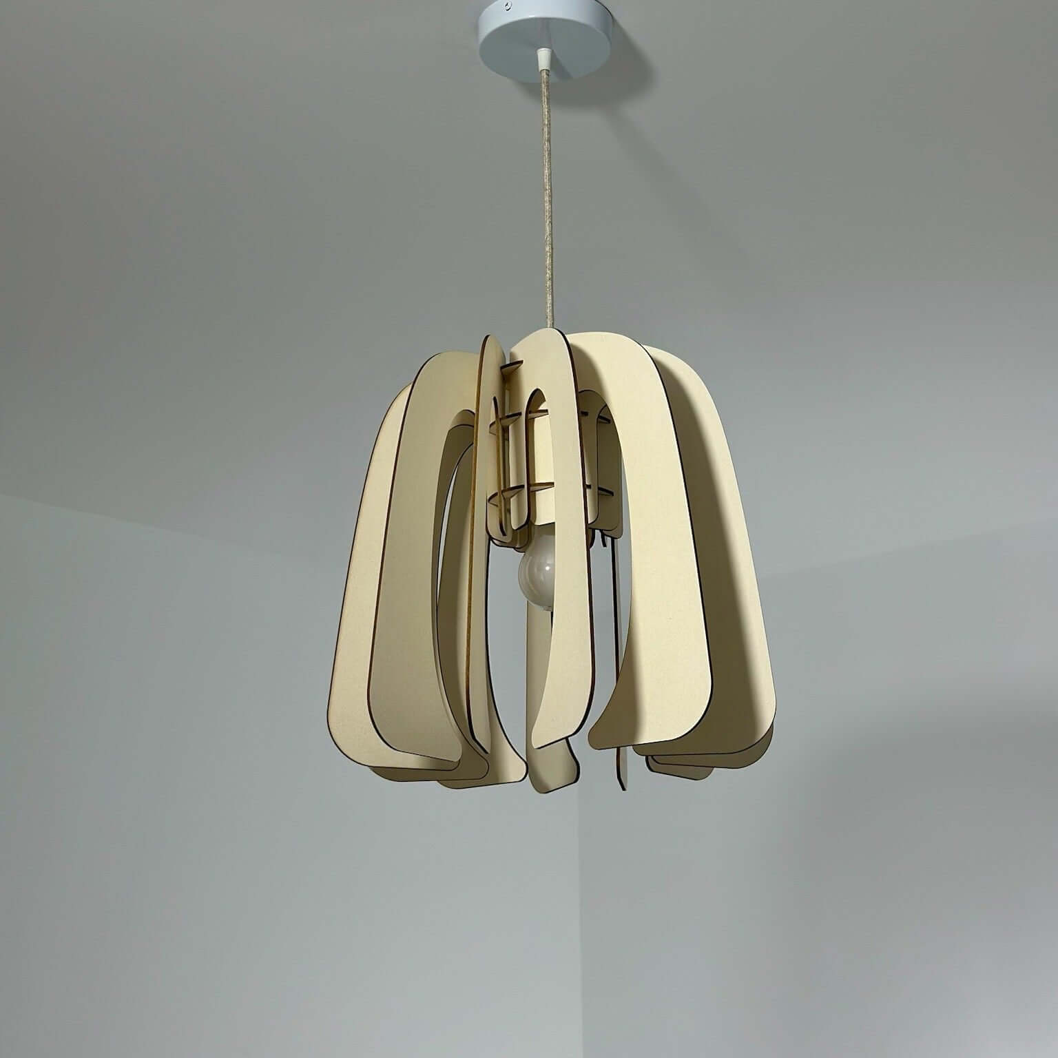 Un luminaire suspendu au design minimaliste et contemporain, composé de lames courbées en matériau naturel de couleur beige clair. La lampe, fixée au plafond par un câble en textile, se distingue par ses formes organiques et épurées, qui apportent une touche moderne à tout intérieur. Le fond blanc met en valeur les lignes élégantes et la finition. 