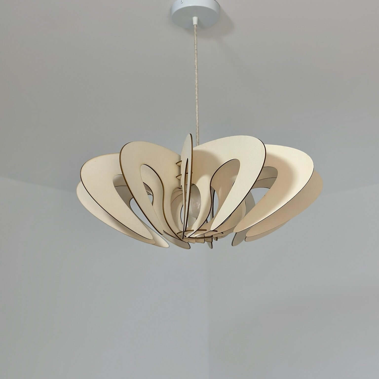 Ce luminaire suspendu est constitué de panneaux de bois clair découpés en formes organiques et courbées, s’assemblant pour créer un design sculptural et élégant. Les découpes en arcs et courbes apportent une esthétique légère et moderne, tandis que le bois naturel confère une ambiance chaleureuse. Il est suspendu au plafond par un fil discret, accentuant son aspect minimaliste et épuré. Ce luminaire est idéal pour compléter une décoration intérieure contemporaine ou scandinave.