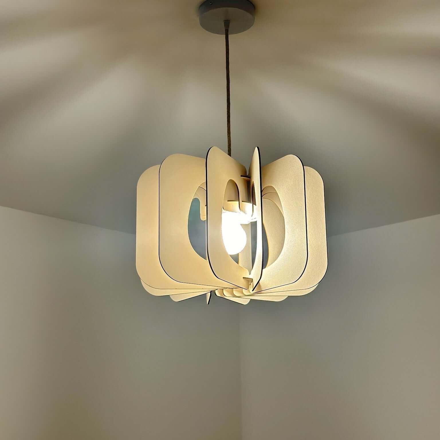 Suspension lumineuse en bois clair avec un design sculptural et ajouré. La lumière diffuse se reflète harmonieusement sur le plafond, créant un jeu d'ombres élégant. Une pièce idéale pour ajouter une touche contemporaine et chaleureuse à tout intérieur.